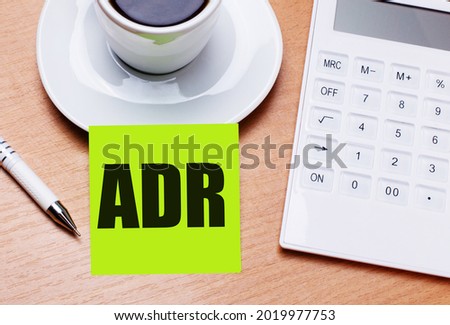 The wooden table has a white cup of coffee, a pen, a white calculator, and a green sticker with the text ADR Alternative Dispute Resolution. Business concept