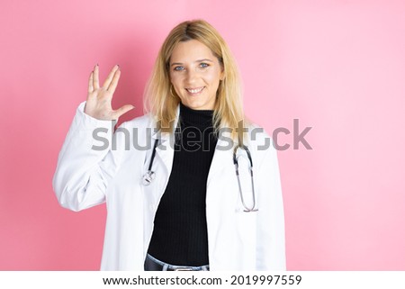Young blonde doctor woman wearing stethoscope standing over isolated pink background doing hand symbol