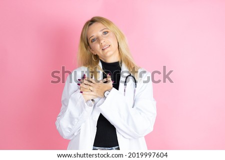 Young blonde doctor woman wearing stethoscope standing over isolated pink background smiling with her hands on her chest and grateful gesture on her face.