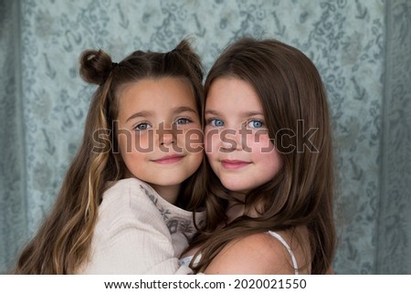 Selective focus medium portrait of beautiful smiling little girl cuddling in the arms of her pretty older sister seen against blue background	 Royalty-Free Stock Photo #2020021550