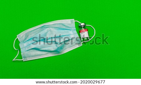 Conventional 3-layer hygiene face mask with elastic ear hook beside sealed glass capsule of covid-19 vaccine as world modern infection prevention against virus or disease outbreak