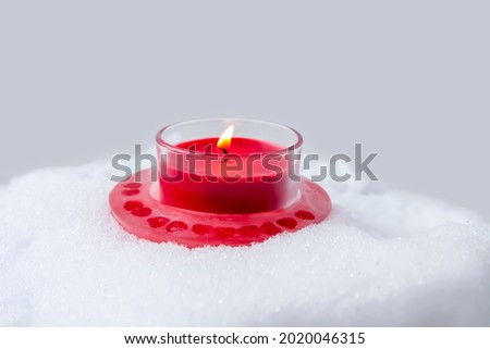 Burning red Christmas candle on fresh snow background.