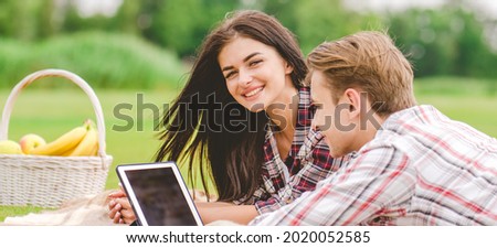 The happy man and woman with a tablet lay on the ground