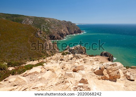 View of rocky mountain towering over Atlantic ocean, skyline in distance and bunch of stones in front at Cape Roca, Portugal
