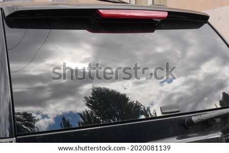 Slightly blurry and distorted reflection of the sky with clouds, trees and wires in the glass of the car. Abstract look with dramatic sky for creative design. Close-up.
