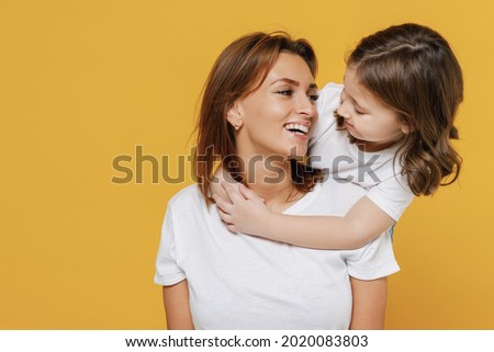 Happy woman in white t-shirt have fun with cute child baby girl 5-6 years old stand behind Mommy little kid daughter isolated on yellow orange color background studio. Mother's Day love family concept