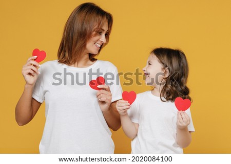 Happy woman in basic white t-shirt have fun and child baby girl 5-6 years old hold heart. Mom mum little kid daughter isolated on yellow orange color background studio Mother's Day love family concept