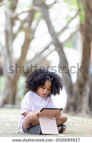 little African American curly hair girl a tablet sitting on the ground communicating online learning Sitting in the park under the trees, there was curious curiosity about the lessons tablets in hand.