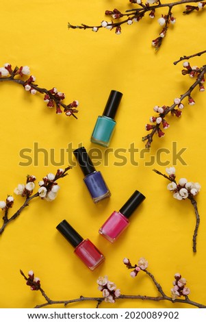Nail pilish bottles and beautiful white flowering branches on yellow background. Springtime, beauty concept. Flat lay, top view.