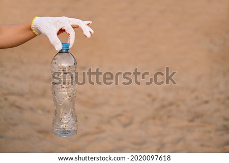 A hand holds a dirty plastic bottle on the background of a sandy beach. The concept of ecological cleaning of the banks.