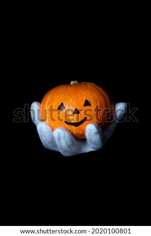 A hand in a white glove holds a pumpkin on a black background for the holiday of Halloween.