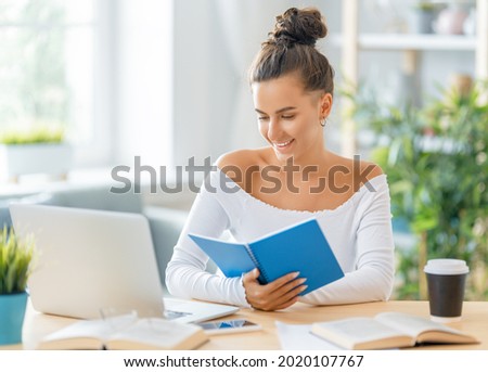 Focused young businesswoman studying online, watching webinar, podcast on laptop, making notes, sitting at work desk. E-learning concept.