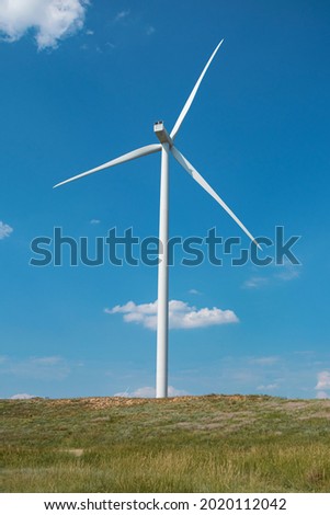 windmill on the background of the cloudy blue sky. Concept of alternative energy production from wind. Modern windmill with full-length blades. High quality photo