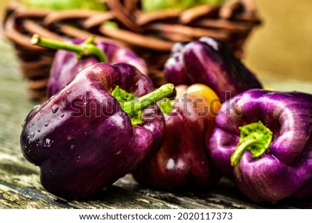 fresh whole purple bell peppers on rustic wood tabletop with wicker basket Royalty-Free Stock Photo #2020117373