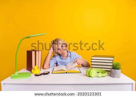 Photo of tired upset schoolboy wear blue shirt sitting desk having read many book isolated yellow color background