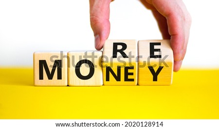 More money symbol. Businessman turns wooden cubes and changes the word 'More' to 'Money'. Beautiful yellow table, white background, copy space. Business and more money concept.