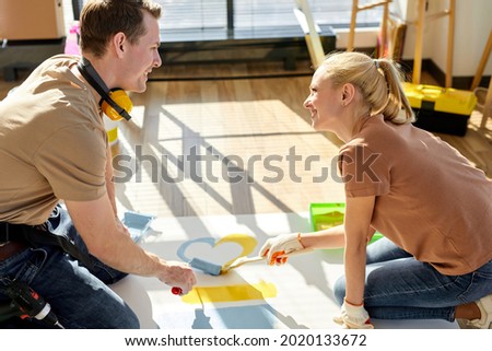 Creating love on paper. Friendly family couple sit on warm floor paint bright picture, shape of heart. caucasian young couple with using brush for painting, spend weekend at new home. side view