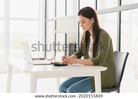 Concentrated young business woman freelancer manager accountant counting funds, savings, money using calculator in office. Woman paying bills, economizing. Economy and finances concept Royalty-Free Stock Photo #2020155869