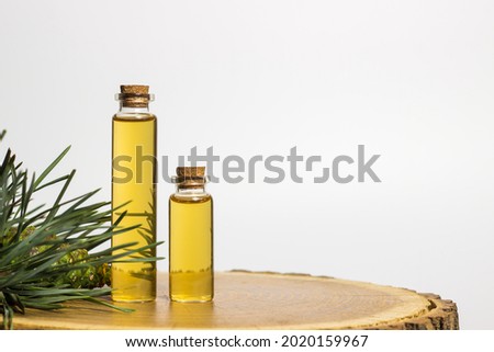 Two glass jars with yellow oil and pine plant extract on a tree cut. White background. Place for inscriptions and text.