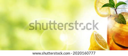 Fresh cold iced tea in summer with lemon and mint in a frozen glass. Horizontal close up with bright green bokeh background and space for text.