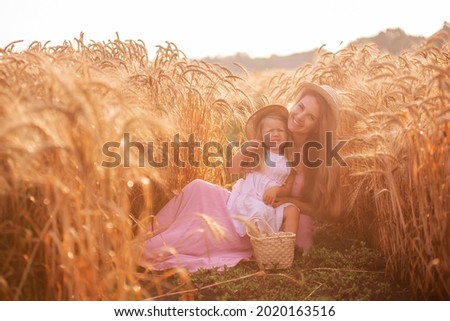 Close-up portrait of mother with daughter in straw hats in wheat field with dew drops. Young woman have fun with girl, tickle each other with golden ears of rye, laugh hug kiss each other. Countryside