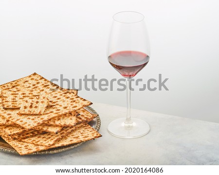 Stylish vintage composition on a plain white background. Matzah on a plate and a glass of red wine. Minimalism. There are no people in the photo. Restaurant, hotel and advertising business.