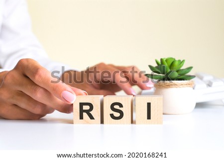 female hand holds a block with the letter S from the word RSI. the word is located on a white office table on the background of a white keyboard. financial, marketing and business concepts