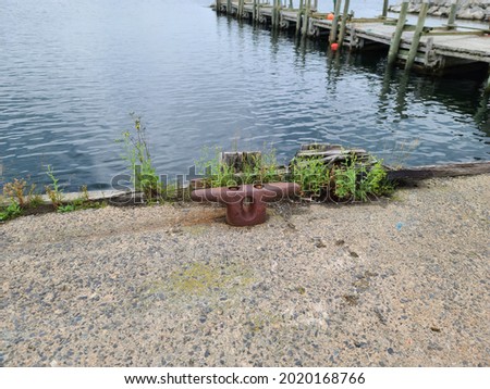 A boat docking station, or a cleat, that is used to tie up boats to keep them attached to the pier. Its metal, red, and in the shape of a letter T. The wharf is wooden and zig zags.