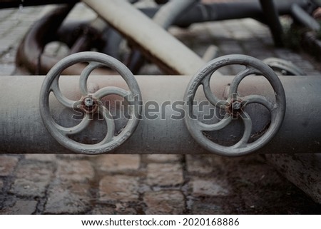 Pipe equipment on a heavy industry site. Two round faucets or valves with spiral pattern on a grey water tube. 