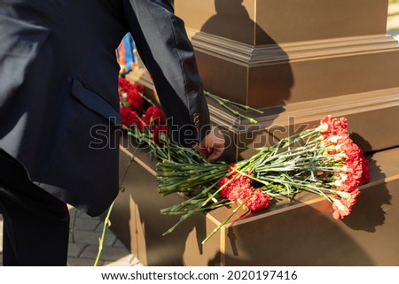 A hand puts carnations on the memorial. Flowers on the monument. Memorable date. The symbolic flower is red.