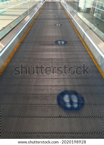 Social distancing footprint marks and the travelator belt in the airport. COVID-19 signs.