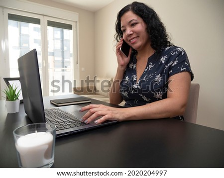 Young caucasian woman with deep hair working from her living room on a laptop on a black table with a white candle, her phone and a credit card with a black notebook