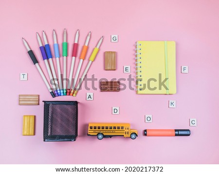 School bus, pencils, plasticine, notebook and wooden cubes with letters on a pink background, top view close-up.