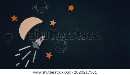 Rocket, moon, stars and painted planets on the left on a black background with space for text on the right, close-up top view.