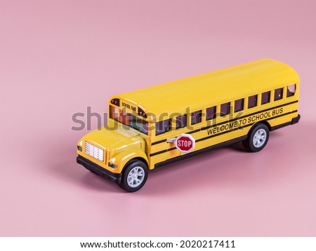 An isolated toy school bus stands on the right on a pink background diagonally, side view close-up. Concept back to school.