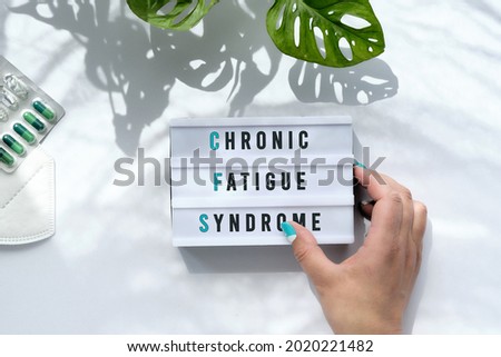 Text Chronic Fatigue Syndrome or CFS on light box in hand. Long illness awareness design. Off white background with trendy monstera leaves and long shadows. Flat lay, top view overhead. Royalty-Free Stock Photo #2020221482