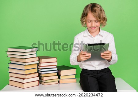 Photo of little cute blond boy hold tablet with book wear white shirt isolated on green color background