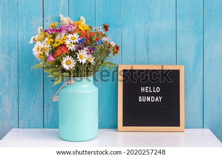 Happy Sunday words on black letter board and bouquet of bright wildflowers in tin can vase on table against blue wooden wall. Concept Hello Sunday. Royalty-Free Stock Photo #2020257248