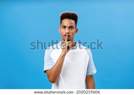 Waist-up shot of bothered and pissed good-looking african man with afro hairstyle frowning from irritation and annoyance demanding shut up keep secret and shushing at camera over blue wall Royalty-Free Stock Photo #2020259606