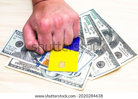 a man holds a stack of hundred-dollar bills and a credit card lying on the table with his fist. High quality photo