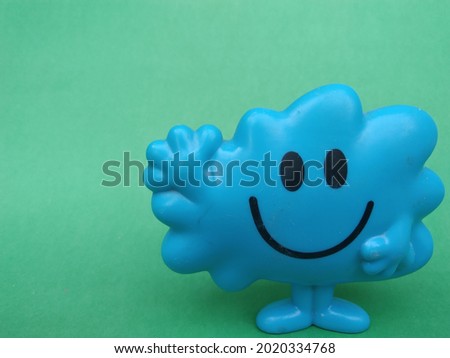 a smiling blue toy waving his hand on a green background .with an empty space on the left