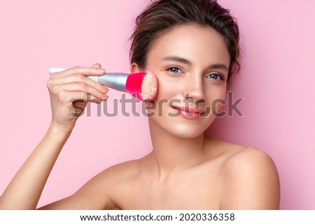 Woman applying powder on the face using makeup brush. Photo of woman with perfect makeup on pink background. Beauty concept