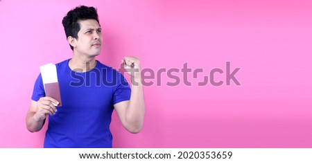 Asian man holding passport and thinking about something on pink background in studio With copy space.