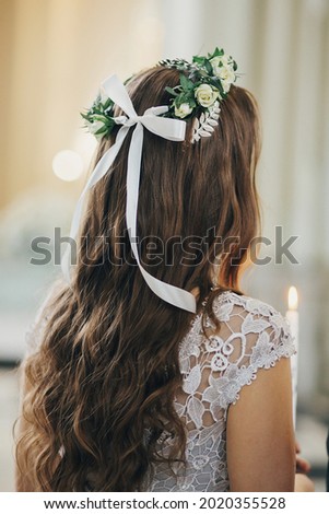 Stylish bride in floral crowns holding candle during holy matrimony in church. Wedding ceremony in cathedral. Classic spiritual wedding bride with burning candle, back view