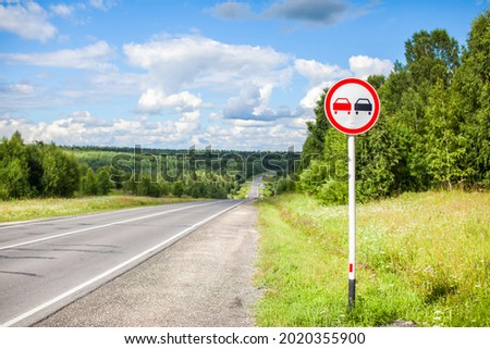A road sign Overtaking is prohibited on a suburban highway through the forest on a sunny summer day.