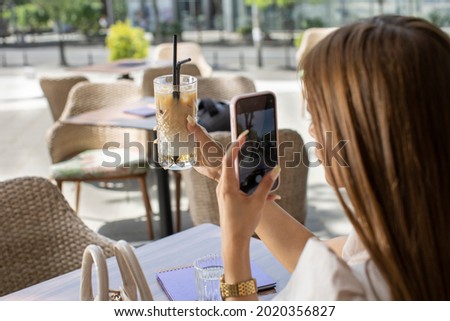 Woman taking photo, with her smartphone, of her iced coffee in the cafe bar