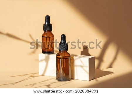 Mock-up of two glass dropper bottles standing on wooden geometric stand. Hard shadows from branch fall on surface of object. Concept of 3d podium for demonstrating cosmetic packaging.
