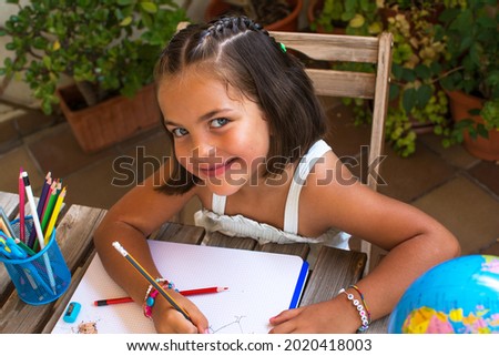 Girl Back To School.
Little Girl Doing Homework In The Courtyard Of Her House. 6-year-Old Girl With Blue Eyes Drawing With Colored Pencils.