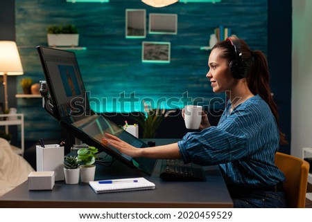 Graphic software editor with headphones working on photography project using touchpad computer monitor sceen display. Woman at workplace doing photo retouching with modern interface