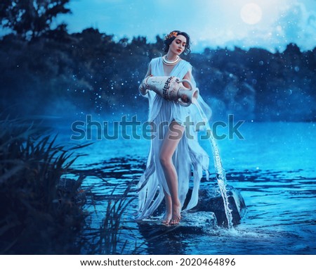 Fantasy woman Greek goddess zodiac sign Aquarius holds vintage earthenware jug in her hands and pours water into river. Background lake blue water, magic night, moon light stars. Astrology concept Royalty-Free Stock Photo #2020464896